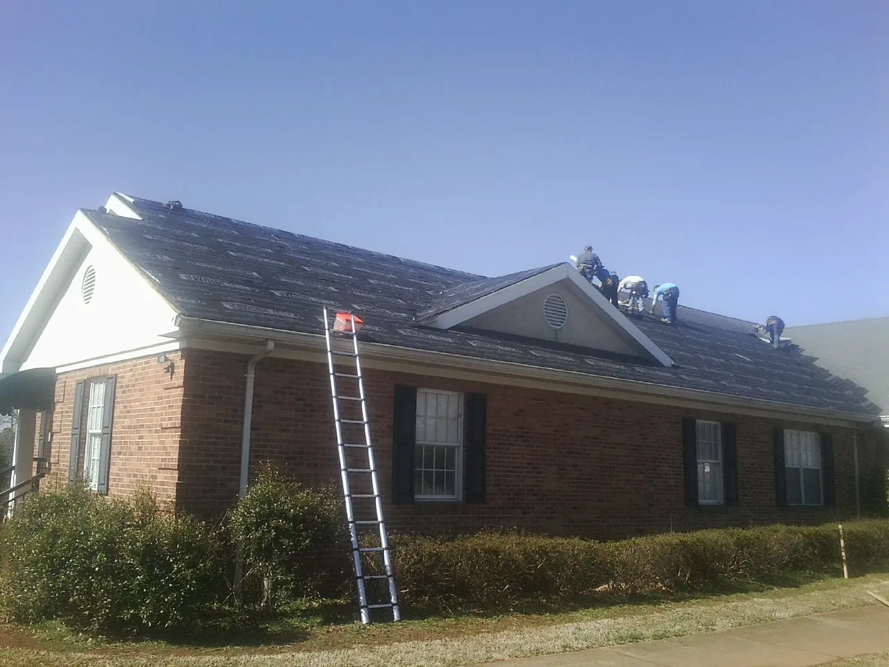 Crew tearing shingles off a brick ranch roof with a ladder set — Emergency Roof Repair work by our crew in Cutler