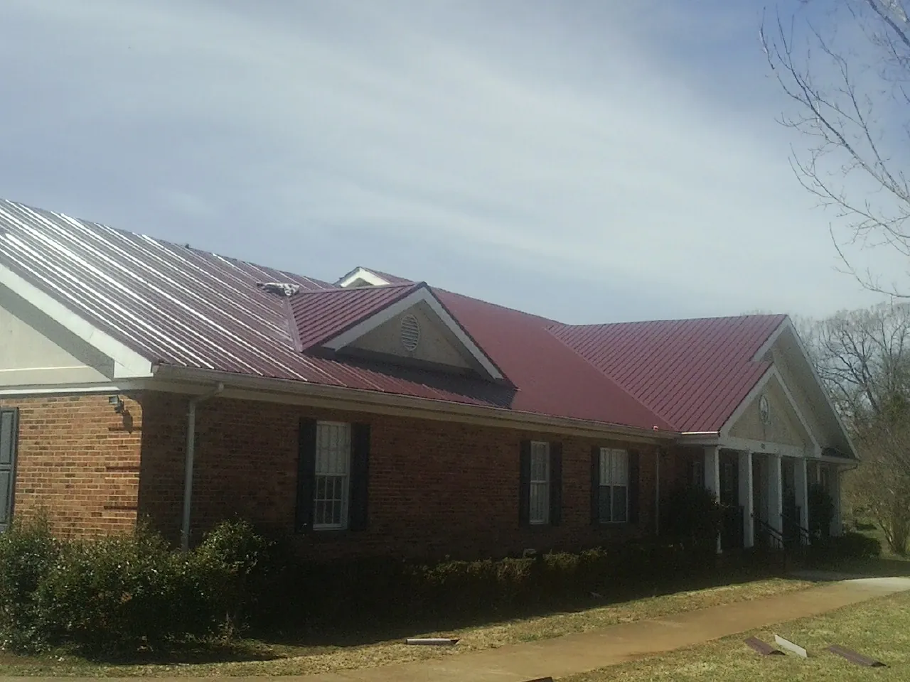 Red metal roof with gabled entries on a long brick building, from a Hail Damage Roof Repair job in Cutler