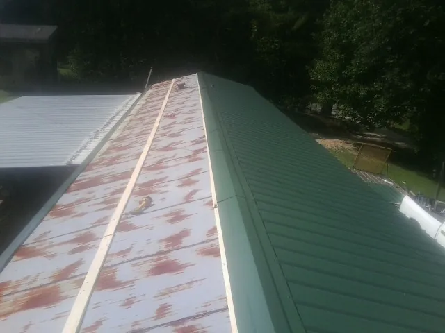 Old rusted panels beside newly installed green metal roofing — Wind Damage Roof Repair by Roofing Brothers in Cutler