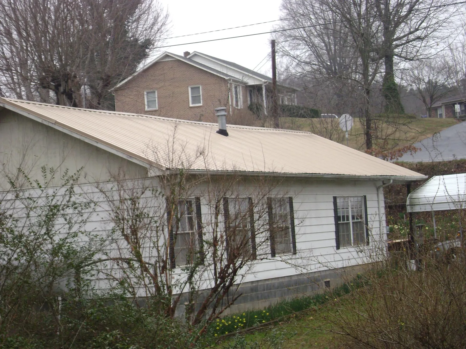 Tan metal roof on a white sided house set into a hillside — Commercial Roofing by Roofing Brothers in Cutler