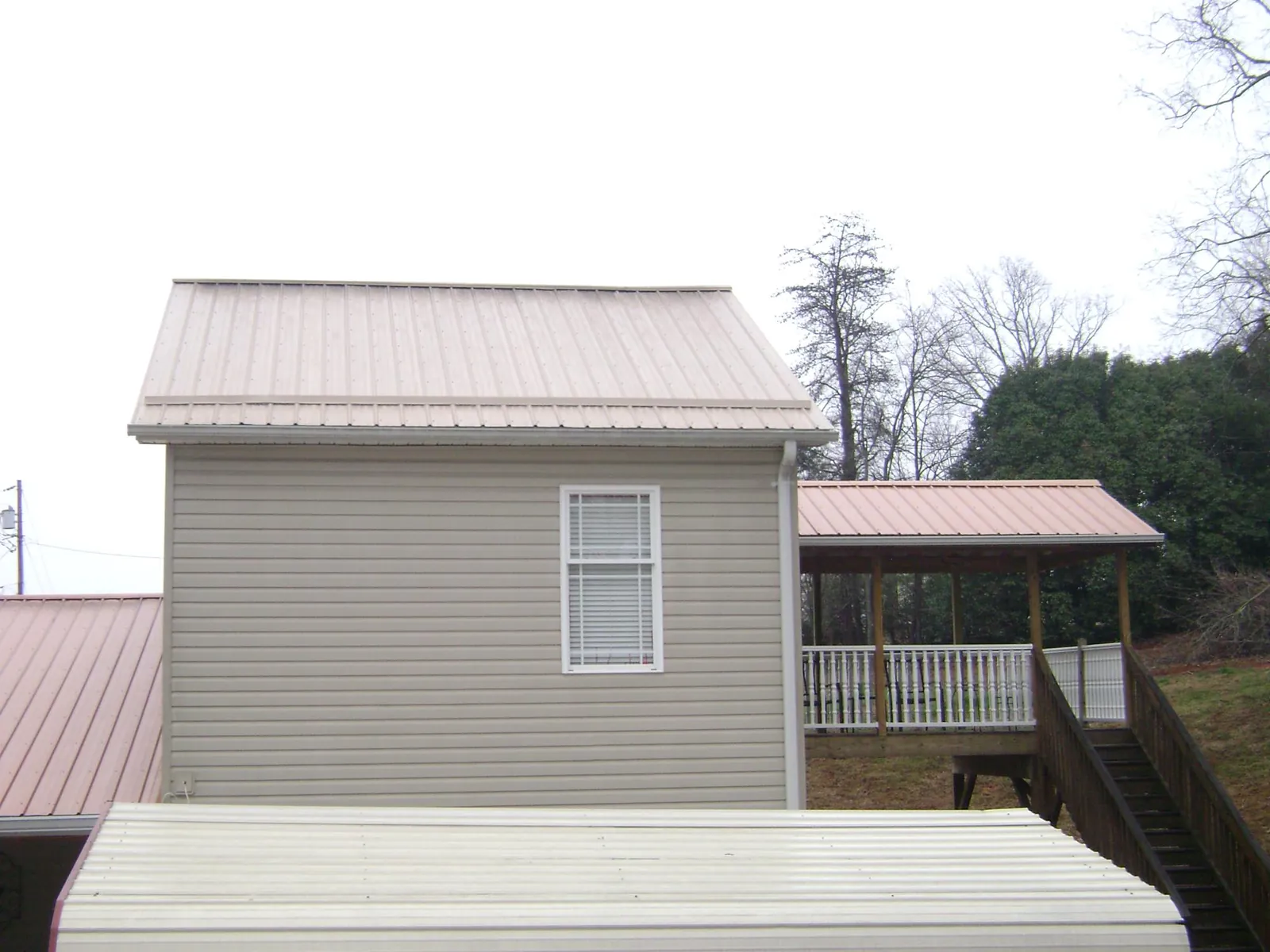 Tan metal roofs on a two story addition and attached porch, from a Roof Replacement job in Cutler